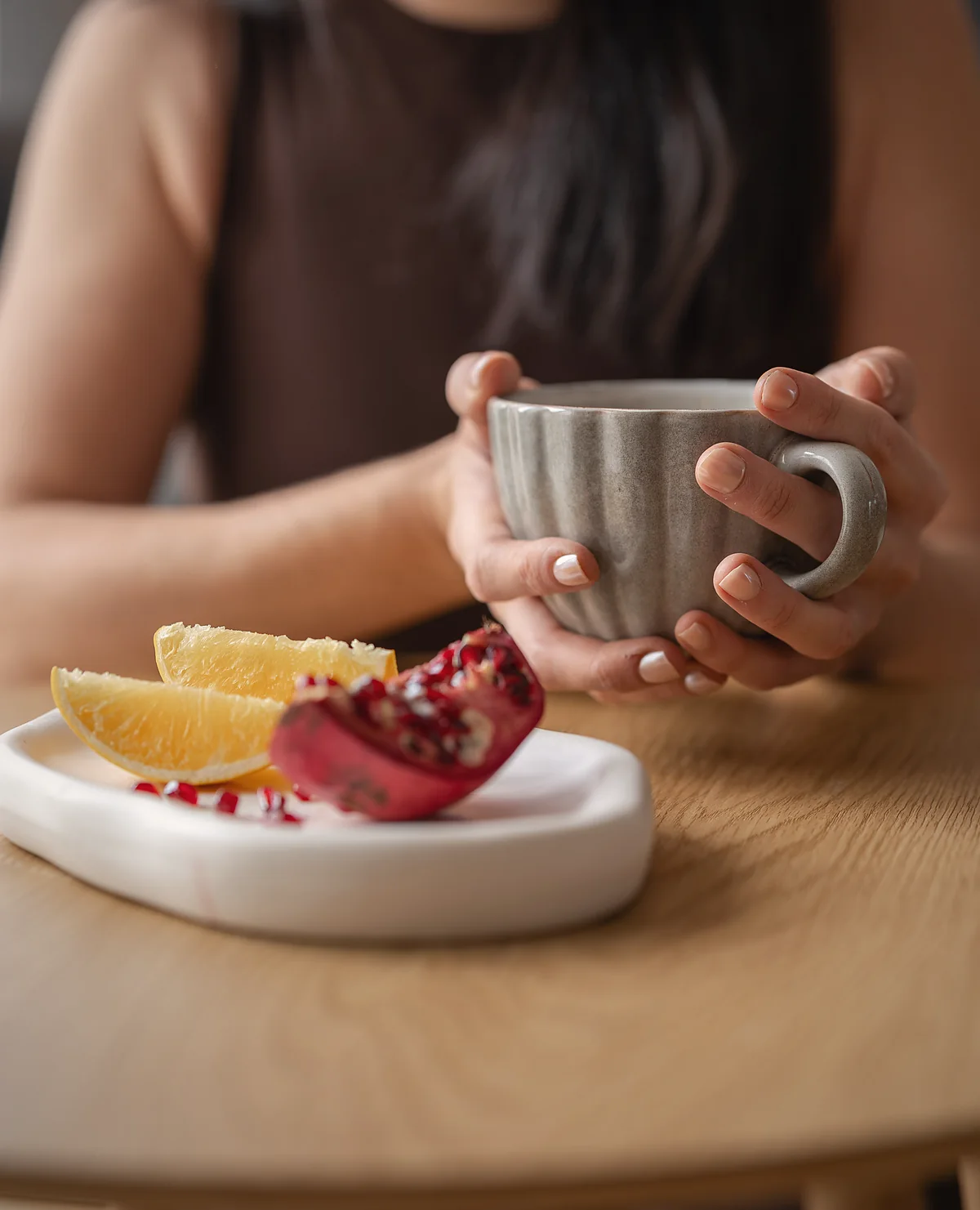 Hände um eine Tasse, daneben Orange und Granatapfel